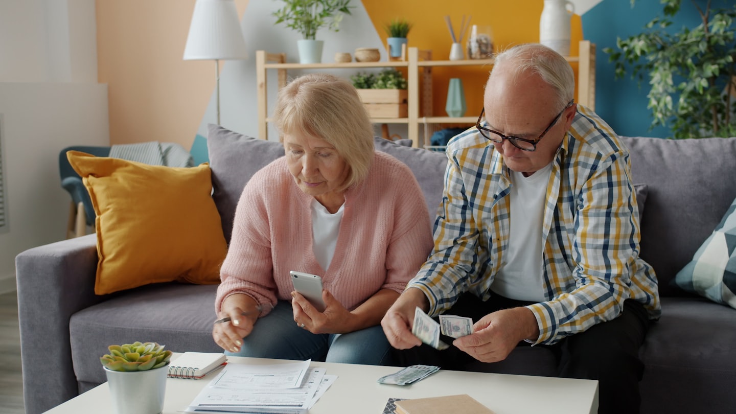 Elderly couple managing finances on a living room sofa.