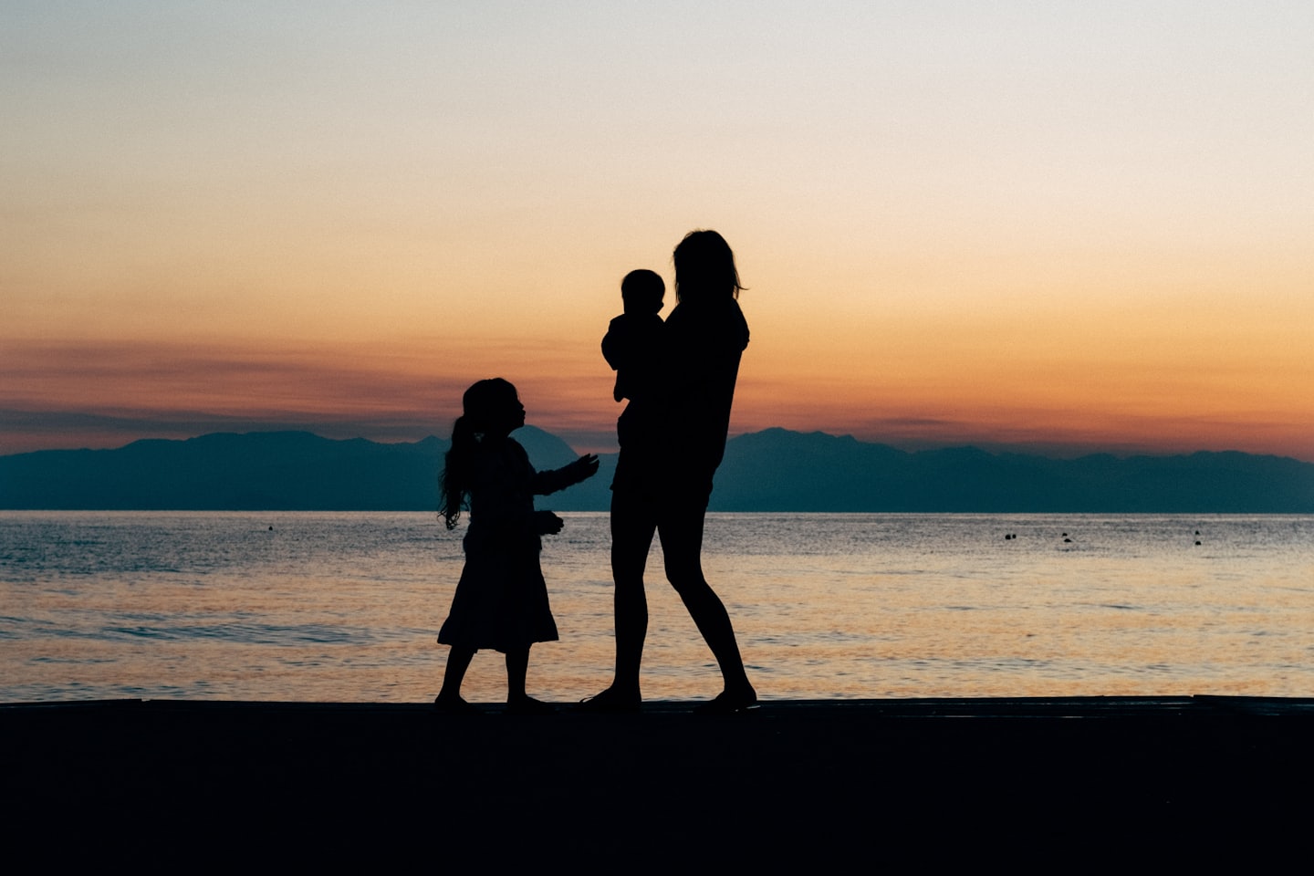 Family silhouetted against a sunset over water.