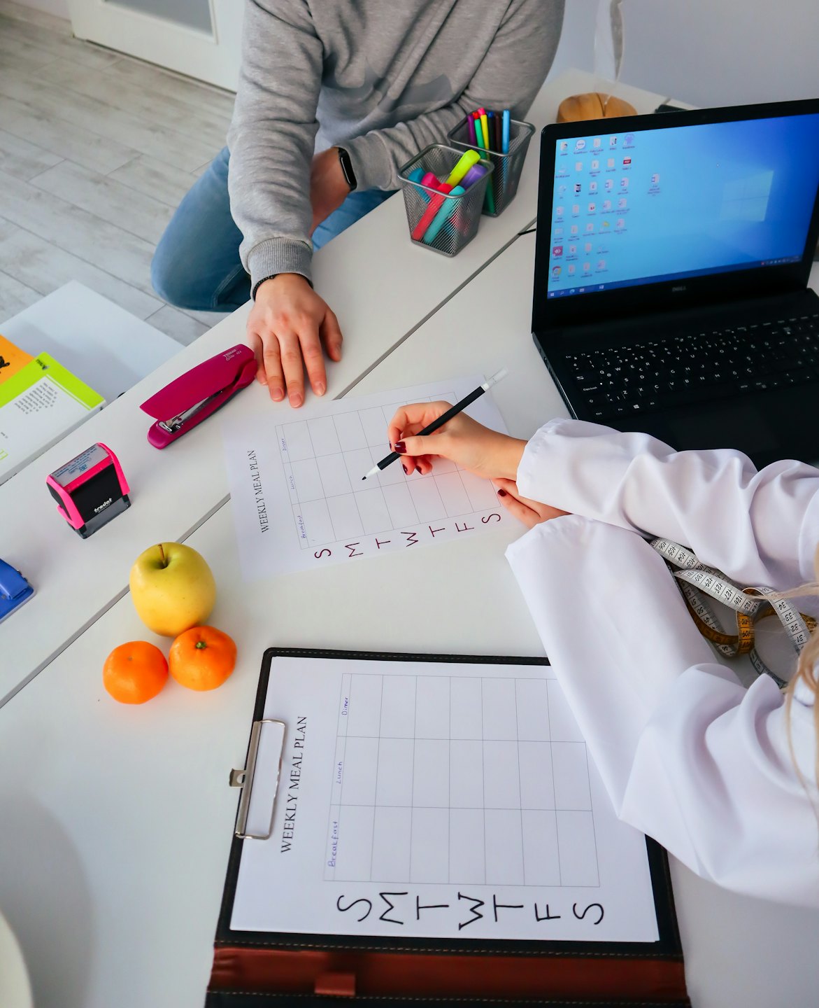 Professional guides client through weekly meal plan at a desk.