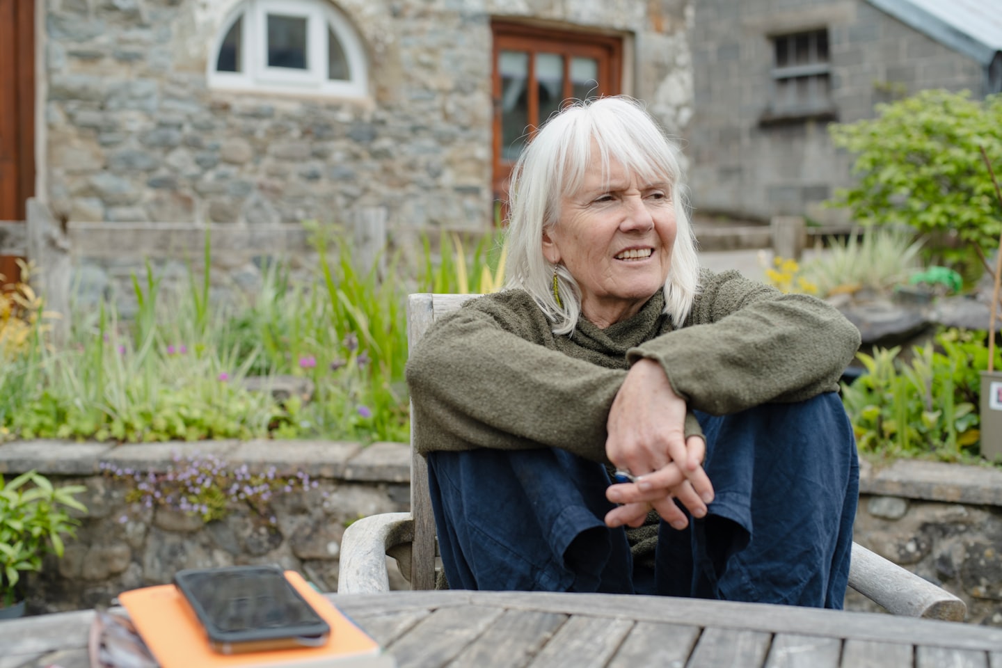 Woman in green sweater uses smartphone at outdoor table.